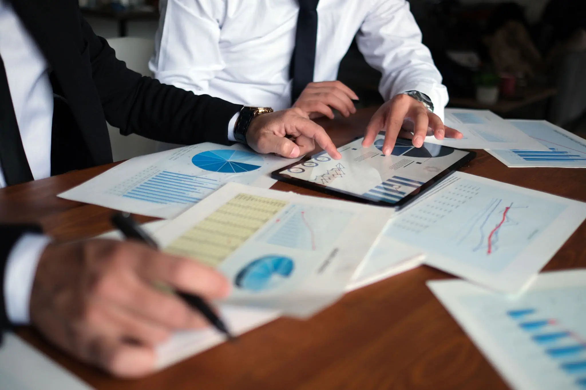 Business meeting discussing charts and data on tablet and papers.